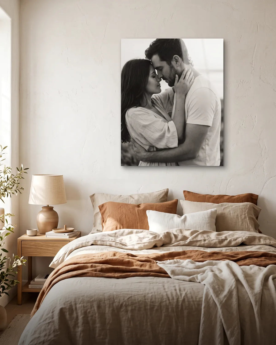 Black-and-white photo of a couple embracing on a frameless metal print above a sunlit bed